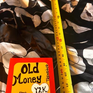 May include: A black and white floral patterned garment with a yellow measuring tape showing a length of 22 inches. A card with the words "Old Money" and "Y2K" is also visible.