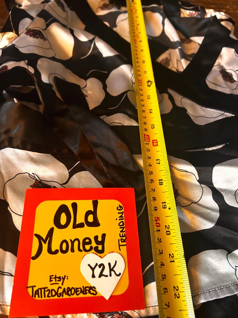 May include: A black and white floral patterned garment with a yellow measuring tape showing a length of 22 inches. A card with the words "Old Money" and "Y2K" is also visible.