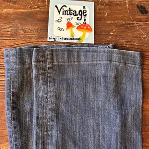 May include: Close-up of blue denim jeans. A small tag with the word "Vintage" and mushroom illustrations is visible. The tag also includes the text "90's, 80's, 70's, 60's" and "Etsy: TATTOOGARDENERS".