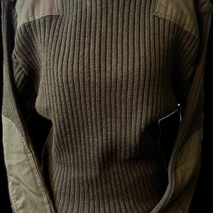 May include: Olive green ribbed knit sweater with reinforced shoulder and elbow patches. The sweater has a high, ribbed neckline and ribbed cuffs. The patches are a darker shade of green. The sweater is displayed on a white mannequin.