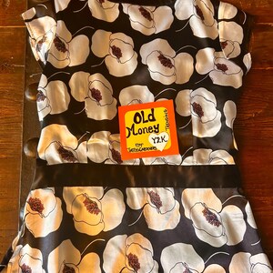 May include: A black and white floral print top with a black satin band. The top features a pattern of large white flowers with red centers on a black background. The tag reads "Old Money" and "Y2K".