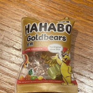 May include: A gold-colored package of HAHABO Goldbears gummy candies. The package features a cartoon bear and the text "The Original since 1922." The package also includes the text "Kids and grown-ups love it so, the happy world of Hahabo!"