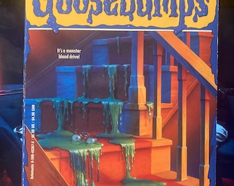 Puede incluir: Un libro de bolsillo titulado "Goosebumps: Monster Blood" de R.L. Stine. La portada presenta una escalera con una sustancia verde viscosa y el texto "It's a monster blood drive!" en un diseño azul y amarillo.