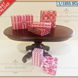 May include: Five miniature gift boxes in various pink and red patterns, including hearts, stripes, and leopard print, are arranged on a dark brown oval table. The table has a pedestal base with ornate carvings. The boxes are labeled "1/12th SCALE" and "BoHeeMeeUhn".