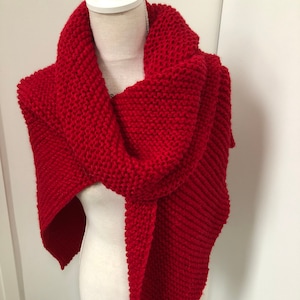 Puede incluir: Una bufanda de punto roja drapeada sobre un maniquí blanco. La bufanda está hecha de un hilo grueso y tiene un punto simple y texturizado.