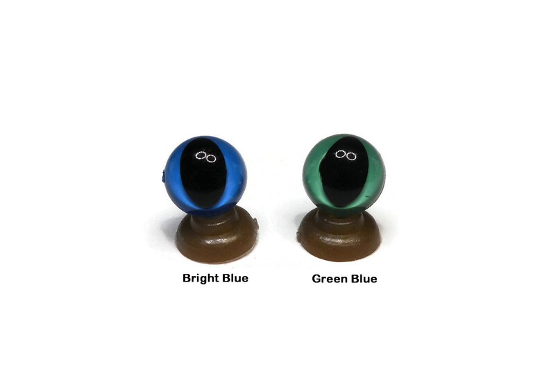 May include: Two plastic doll eyes on display stands. The eye on the left is bright blue with a black pupil. The eye on the right is green blue with a black pupil.
