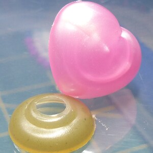 May include: A pink heart-shaped plastic charm and a gold-colored plastic ring with a hole in the center.