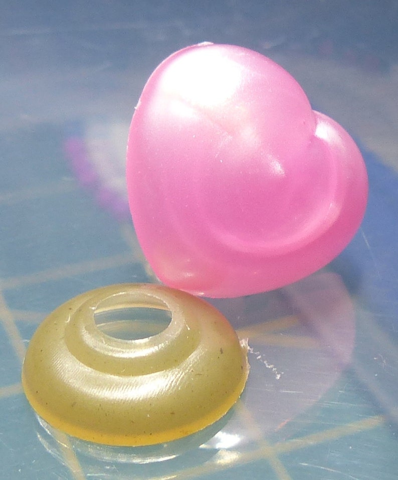 May include: A pink heart-shaped plastic charm and a gold-colored plastic ring with a hole in the center.