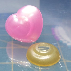 May include: A pink heart-shaped plastic charm and a light brown plastic ring with a hole in the center.