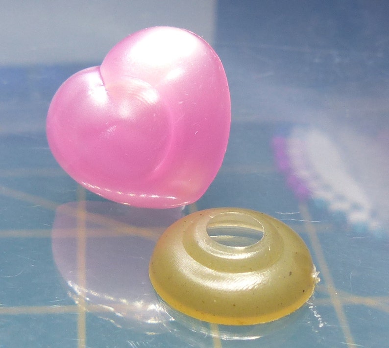 May include: A pink heart-shaped plastic charm and a light brown plastic ring with a hole in the center.