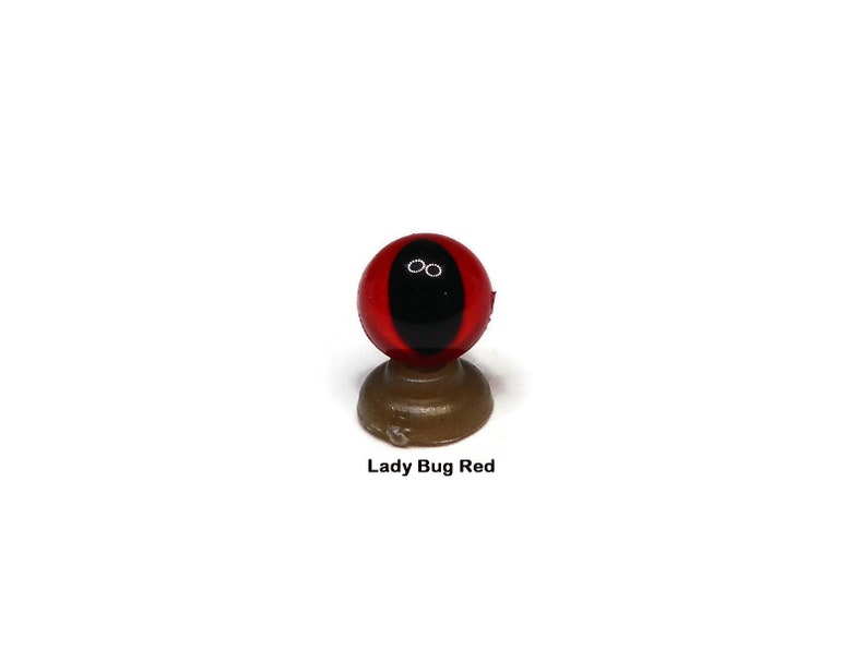 May include: Red and black plastic eye with a black pupil, mounted on a brown base. Lady Bug Red.