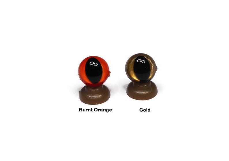 May include: Two plastic doll eyes on display stands. The eye on the left is burnt orange with a black pupil. The eye on the right is gold with a black pupil.