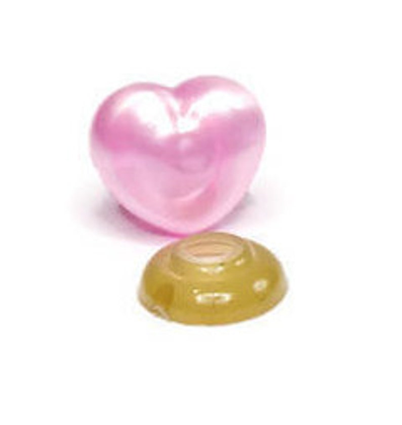 May include: A pink heart-shaped button with a gold-colored plastic base. The button is made of a shiny material and has a smooth surface.
