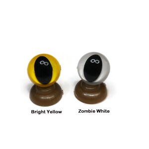 May include: Two plastic safety eyes for crafts, one bright yellow and one white. Both eyes have black pupils.