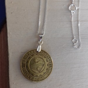 May include: A silver chain necklace with a round pendant featuring the seal of the Central Bank of the Philippines. The seal is gold in colour and features a gear with a sun and a star inside. The text "Bangko Sentral ng Pilipinas" and "1993" are visible on the pendant.