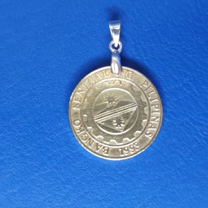 May include: A gold-coloured pendant with a silver bail. The pendant features the seal of the Bangko Sentral ng Pilipinas, which includes the words "Bangko Sentral ng Pilipinas" and the year "1993".