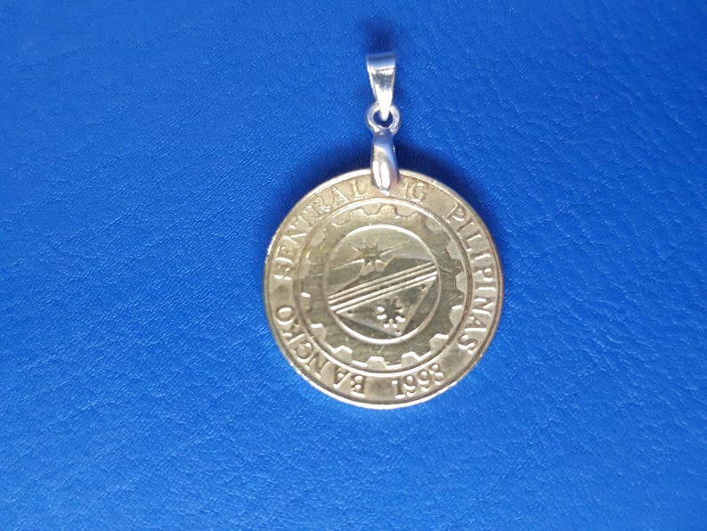 May include: A gold-coloured pendant with a silver bail. The pendant features the seal of the Bangko Sentral ng Pilipinas, which includes the words "Bangko Sentral ng Pilipinas" and the year "1993".