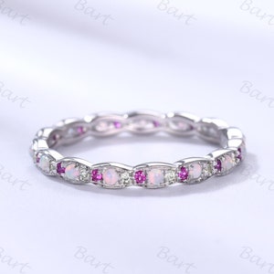 May include: A silver band ring with a row of white opal gemstones and pink sapphires.
