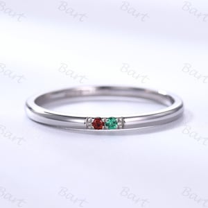 May include: A thin silver band ring with a red and green gemstone set. The ring is simple and elegant.