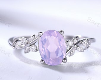 May include: A silver ring with a delicate floral design featuring leaves and small diamonds. The ring has a large oval-shaped light purple gemstone in the center.