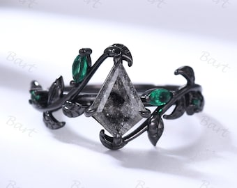 May include: Black engagement ring with a grey diamond and green leaves. The ring is set in a black metal band.