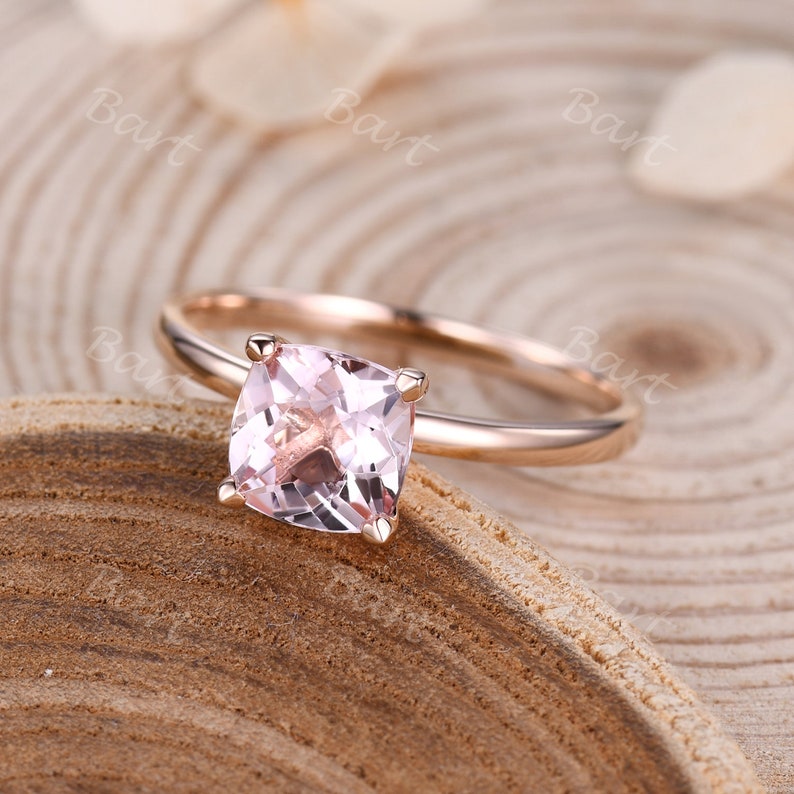 May include: A rose gold engagement ring with a square-shaped pink gemstone.