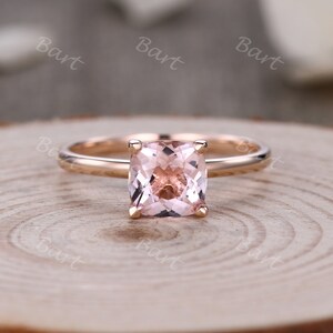 May include: A rose gold engagement ring with a square-shaped pink gemstone.