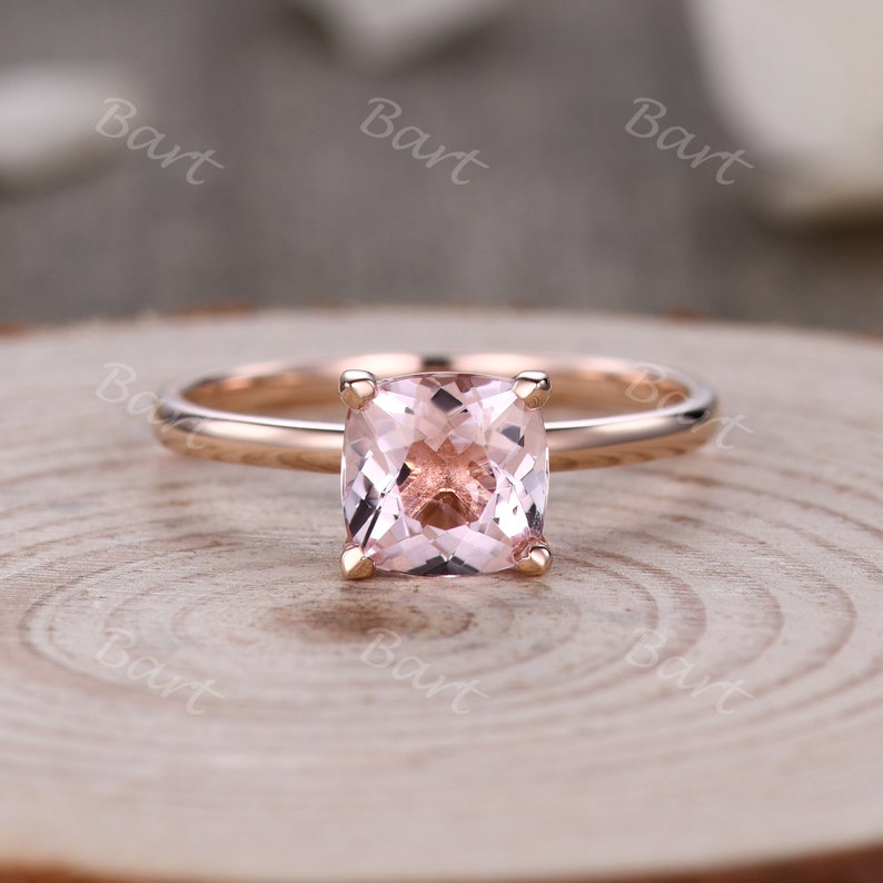 May include: A rose gold engagement ring with a square-shaped pink gemstone.