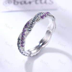 以下が含まれることがあります： ねじれたデザインのシルバーバンドリング。バンドには小さな紫と青の宝石がセットされています。