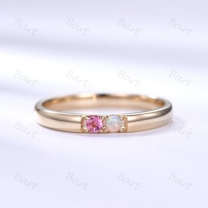 May include: A delicate gold band ring with a pink and white gemstone setting. The ring features a small pink gemstone and a larger white opal gemstone.