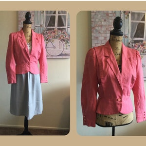 May include: A pink blazer with a single button closure and puffed shoulders. The blazer is on a mannequin wearing a light blue skirt.