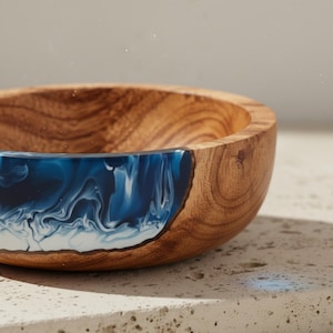 May include: A wooden bowl featuring a blue and white resin inlay. The natural wood grain of the bowl contrasts with the swirling pattern of the resin. The bowl is a decorative item.