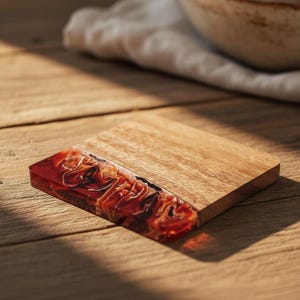 May include: A square wooden coaster with a striking red and black resin inlay. The coaster is crafted from light-coloured wood and has a smooth finish. The resin section features a swirling pattern, adding a decorative touch to the coaster.