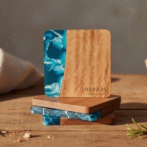 May include: Square wooden coasters with a blue and white resin design. One coaster has the date "01.02.25" and the text "SAID I DO" printed on it. The coasters are stacked on a wooden surface.
