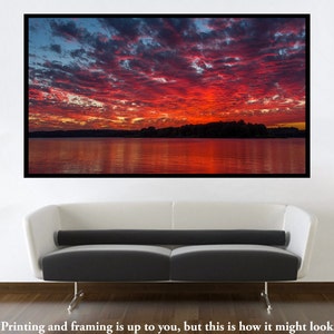 May include: A vibrant red and orange sunset over a still lake, with a dark silhouette of trees on the far shore. The sky is filled with fluffy clouds, reflecting in the water.