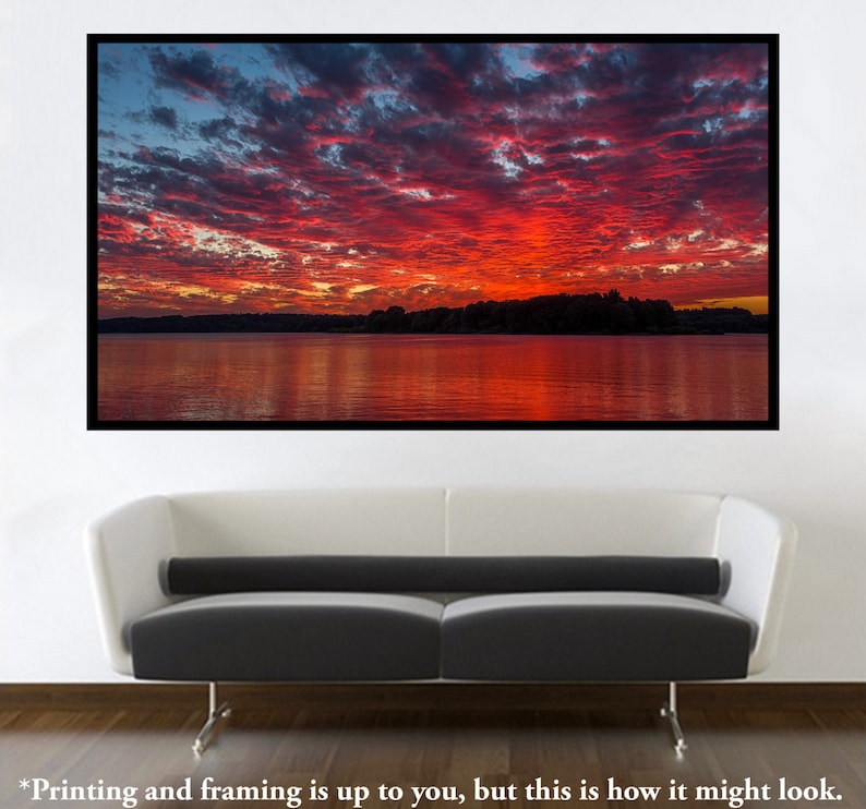 May include: A vibrant red and orange sunset over a still lake, with a dark silhouette of trees on the far shore. The sky is filled with fluffy clouds, reflecting in the water.