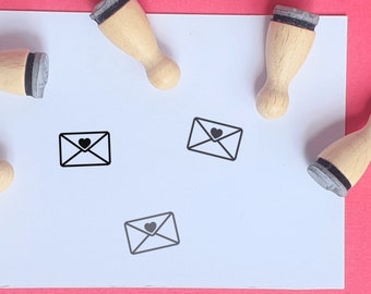 May include: Four wooden stamps with black ink pads and a simple design of an envelope with a heart inside. The stamps are on a white surface.