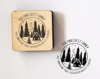 May include: A wooden stamp with a circular design featuring a cabin, trees, and the text "THE PINECREST FAMILY." The stamp also includes the address "945 TIMBERLINE TRAIL, EVERGREEN VALLEY, CO 80439." A stamped impression is also visible.