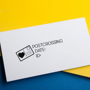 May include: A rectangular white rubber stamp featuring a black graphic of a postcard with a heart icon. The text reads POSTCROSSING, DATE:, and ID:. The stamp is designed for marking mail and correspondence with clear, bold black lettering and lines.