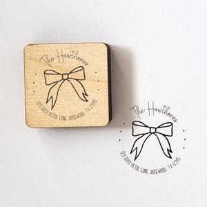 May include: A wooden stamp featuring a bow design, the text "The Hawthorns", and an address. The stamp is square with rounded edges. The design is in black ink.