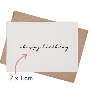 May include: A white greeting card with the black cursive text happy birthday centered on the front, placed over a brown kraft paper envelope. A pink arrow points to the text, accompanied by the measurement text 7 x 1 cm.