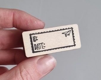 May include: A small wooden tag with a black border and a paper aeroplane graphic. The tag has the words "ID:" and "DATE:" printed on it.