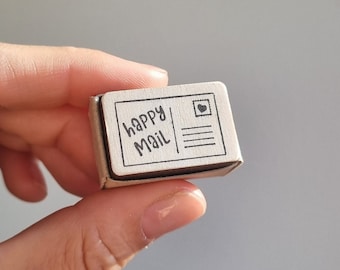 May include: A wooden stamp with a postcard design. The stamp says "happy mail" and has a small heart in the upper right corner.