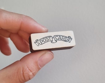 May include: A wooden stamp with the words "POST CARD" in a banner design.