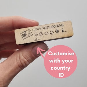 Peut inclure: Un tampon en bois rectangulaire portant l'inscription HAPPY POSTCROSSING et US -. Le motif du tampon comprend une petite icône de carte postale avec un cœur, suivie de symboles météorologiques représentant le soleil, les nuages, la pluie, la neige et un thermomètre.