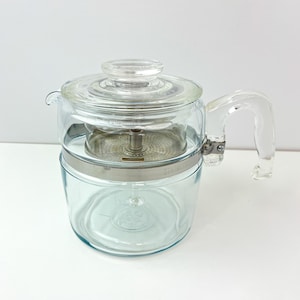 May include: A clear glass percolator coffee pot with a stainless steel band around the middle. The pot has a glass lid and a clear plastic handle.