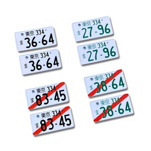 Puede incluir: Una colección de placas de matrícula japonesas en miniatura. Las placas son blancas con texto negro y verde, incluyendo el texto "東京 334" y varias combinaciones de números. Algunas placas tienen una línea diagonal roja.