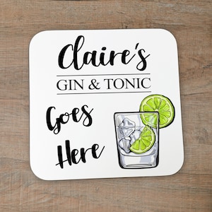 Puede incluir: Posavasos cuadrado blanco con texto negro que dice "Claire's Gin & Tonic Goes Here". A la derecha del posavasos hay un dibujo de un vaso de gin tonic con una rodaja de lima.