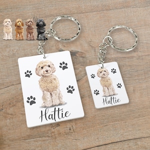 May include: White rectangular keychain featuring a cartoon image of a cream-coloured dog with black paw prints and the name "Hattie" printed on it.