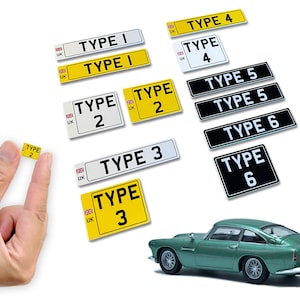 May include: A set of ten different types of UK number plates, numbered 1 through 6, with the text "TYPE" and the number printed on each plate. The plates are in various colours, including white, yellow, and black. The plates are arranged in a grid pattern on a white background. A green toy car is in the lower right corner of the image.